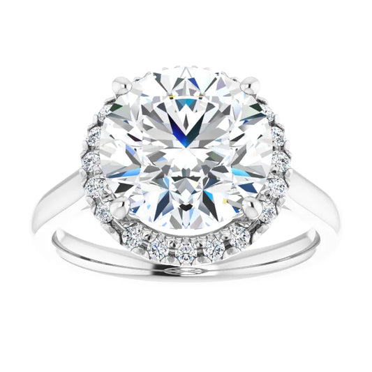 French-set halo-style engagement ring with a round-cut center stone on a white background