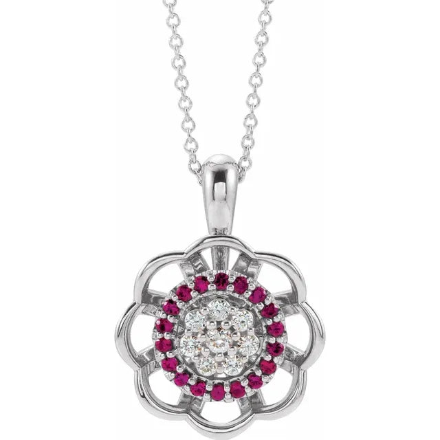 Silver necklace with a flower-shaped pendant. The center of the flower has a cluster of diamonds surrounded by a ring of red rubies. The background is white.