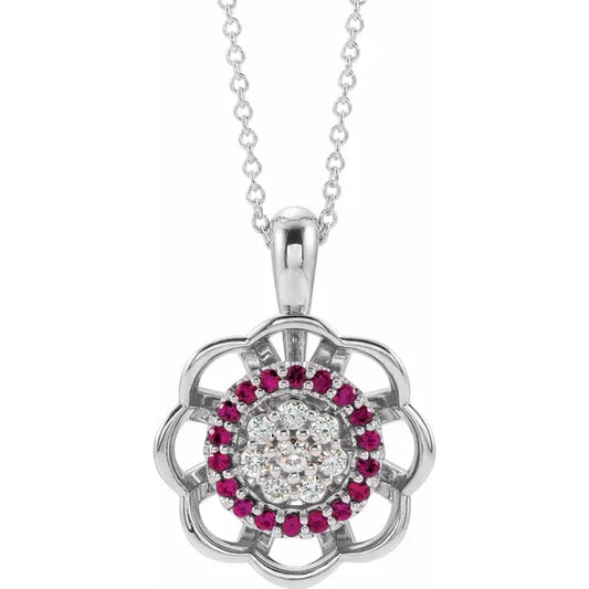 Silver necklace with a flower-shaped pendant. The center of the flower has a cluster of diamonds surrounded by a ring of red rubies. The background is white.